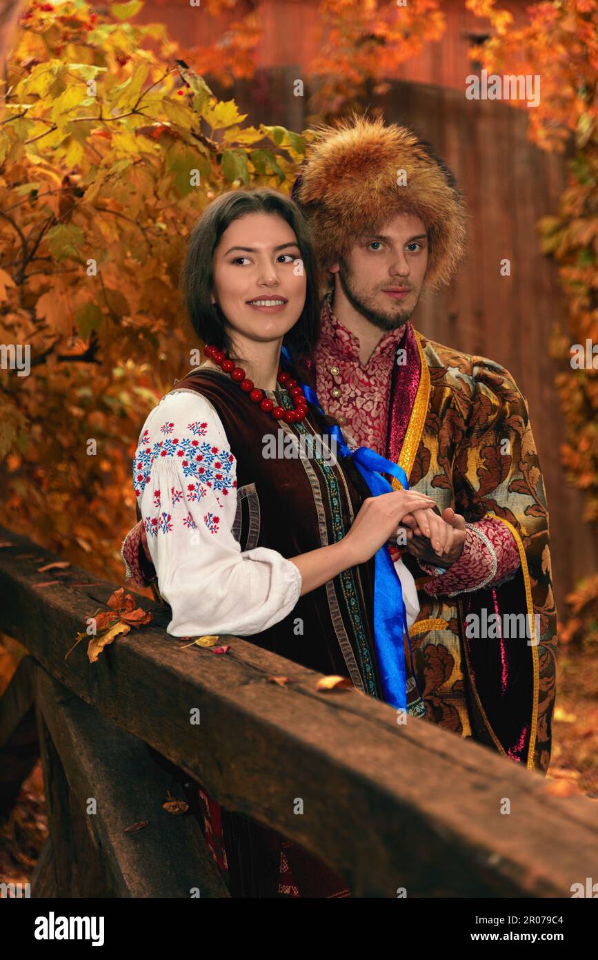 Young couple dressed traditional ukrainian clothing. Serious cossack man and smiling woman in embroidered costumes outdoors. Vintage outfit Stock Photo
