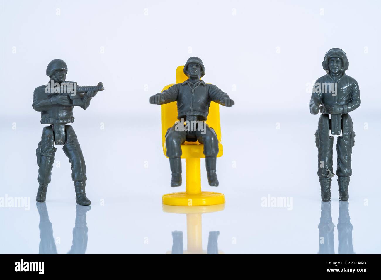 Three toy soldiers with weapons, one of whom is sitting on a chair Stock Photo