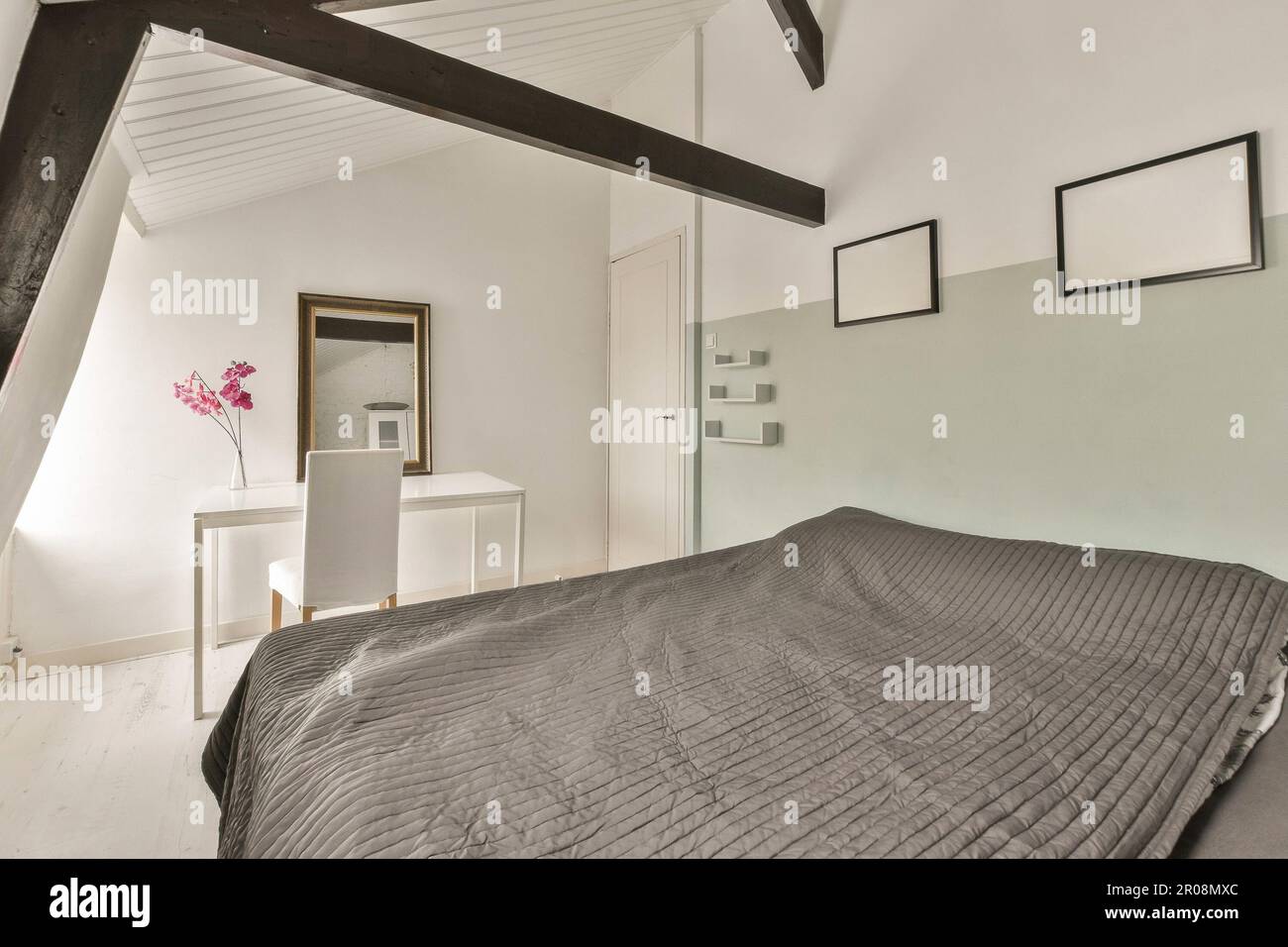 a bedroom with a bed, dresser and mirror on the wall in front of the bed is black and white Stock Photo