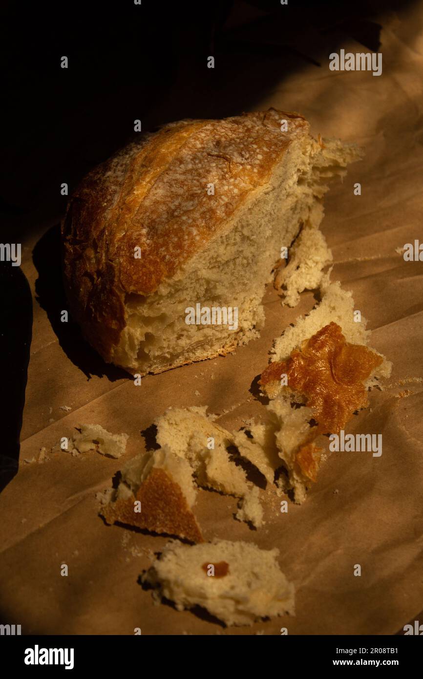 A loaf of sourdough bread cut in half on brown paper in dramatic ...