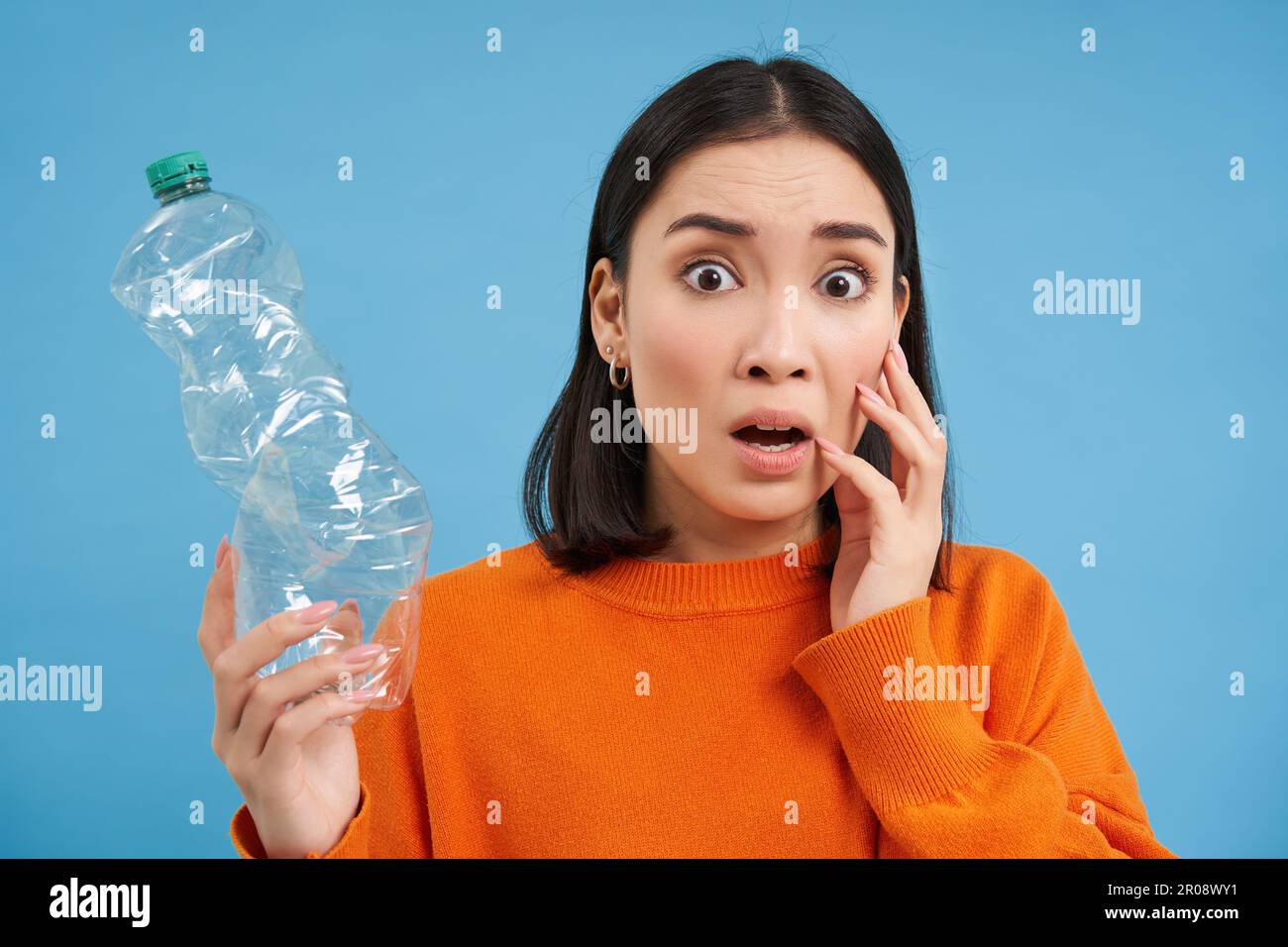 Woman with shocked face, shows empty plastic bottle, looks worried about recycling and sorting