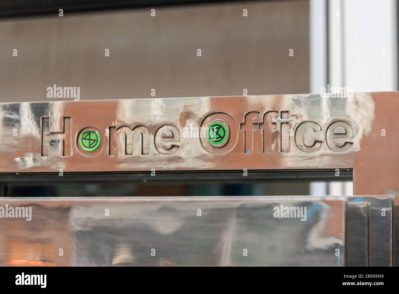 Extinction Rebellion logo stickers stuck to UK government Home Office sign in protest at the Illegal Migration Bill. XR hourglass symbol Stock Photo