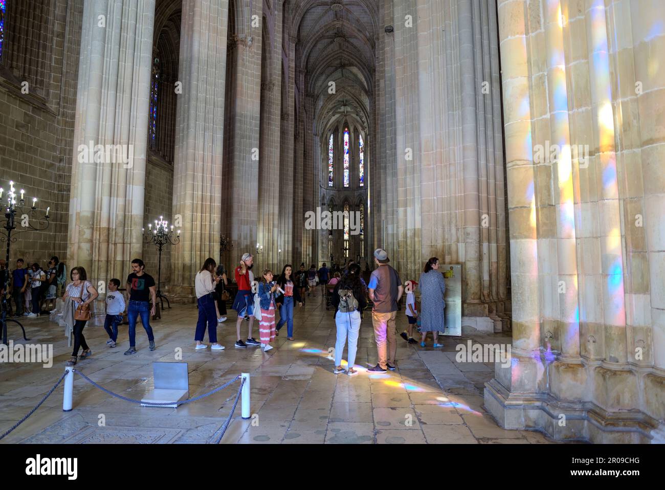 Batalha, Portugal - August 15, 2022: Interior of gothic Monastery showing altar with cross, stained-glass windows, pews and numerous tourists Stock Photo