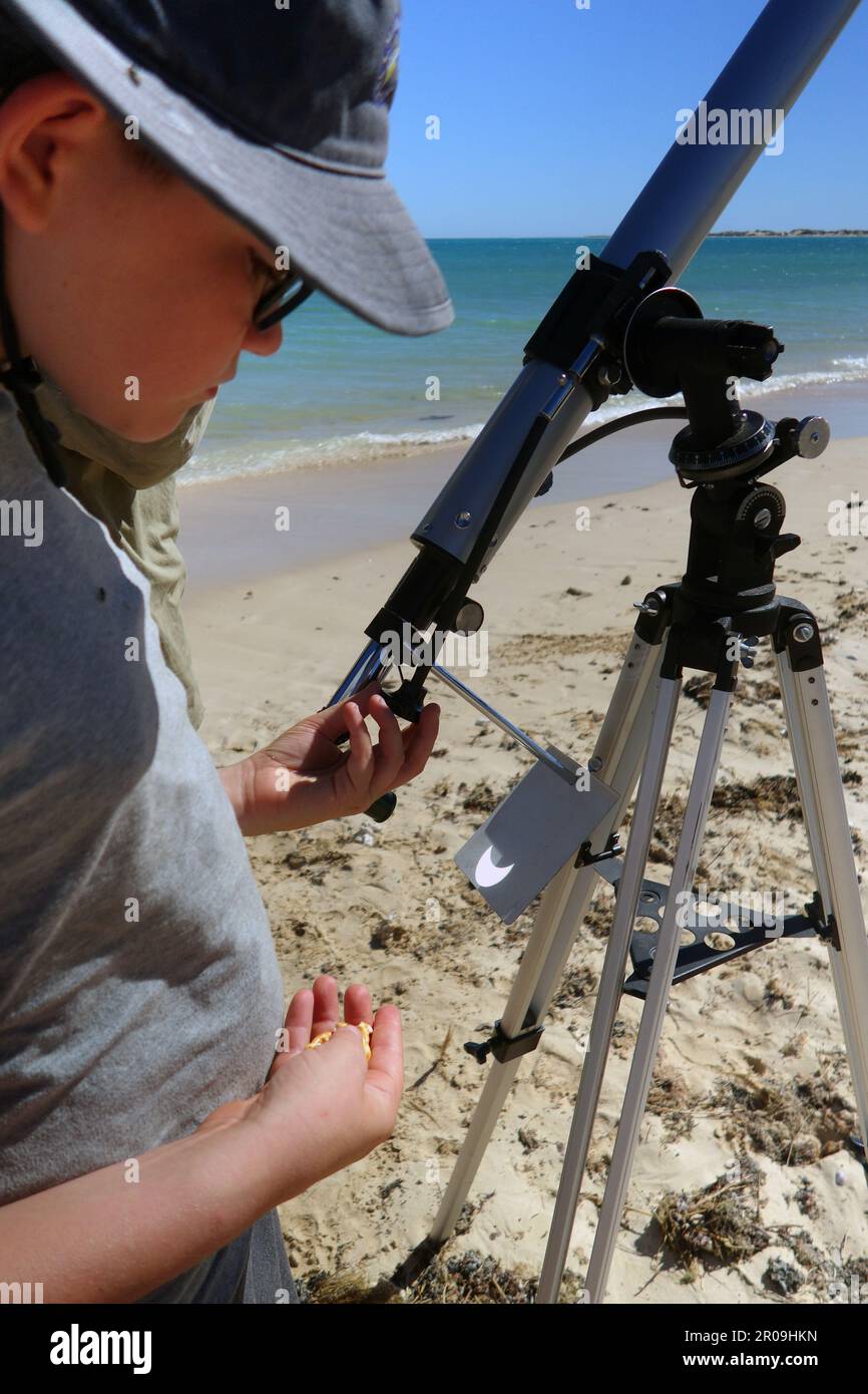 Boy using modified telescope to observe crescent sun during eclipse, on the beach at Ningaloo, 20 April 2023. No MR or PR Stock Photo