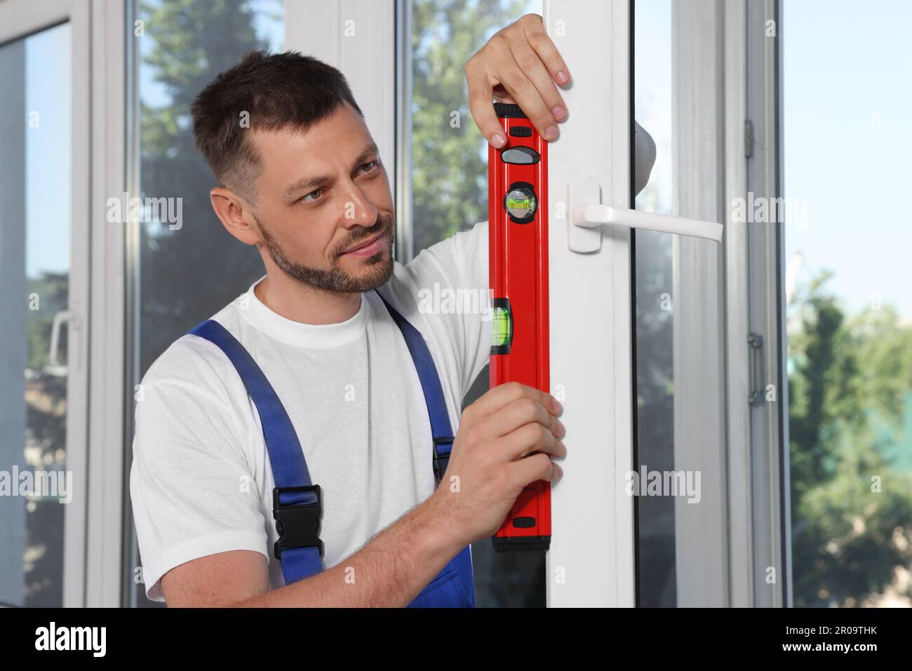 Worker using bubble level after plastic window installation indoors Stock Photo