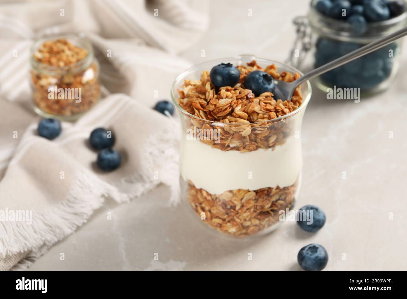 Glass of yogurt with granola and blueberries on grey marble table, closeup Stock Photo
