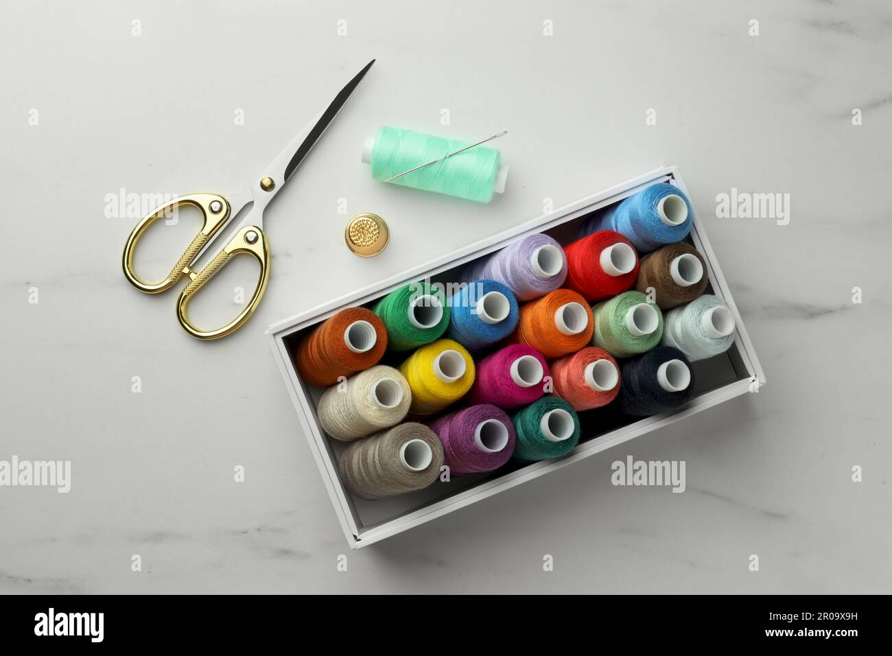Box with colorful sewing threads, scissors and thimble on white marble table, flat lay Stock Photo