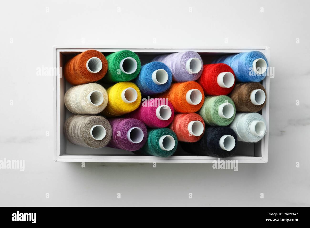 Box with colorful sewing threads on white marble table, top view Stock ...