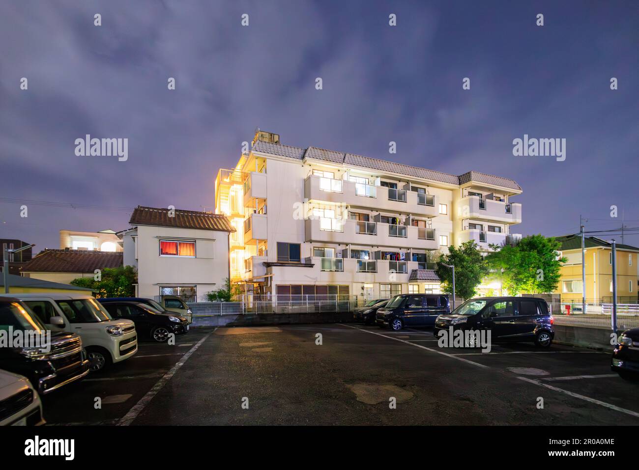 Glowing lights in midrise apartment building by parking lot at night