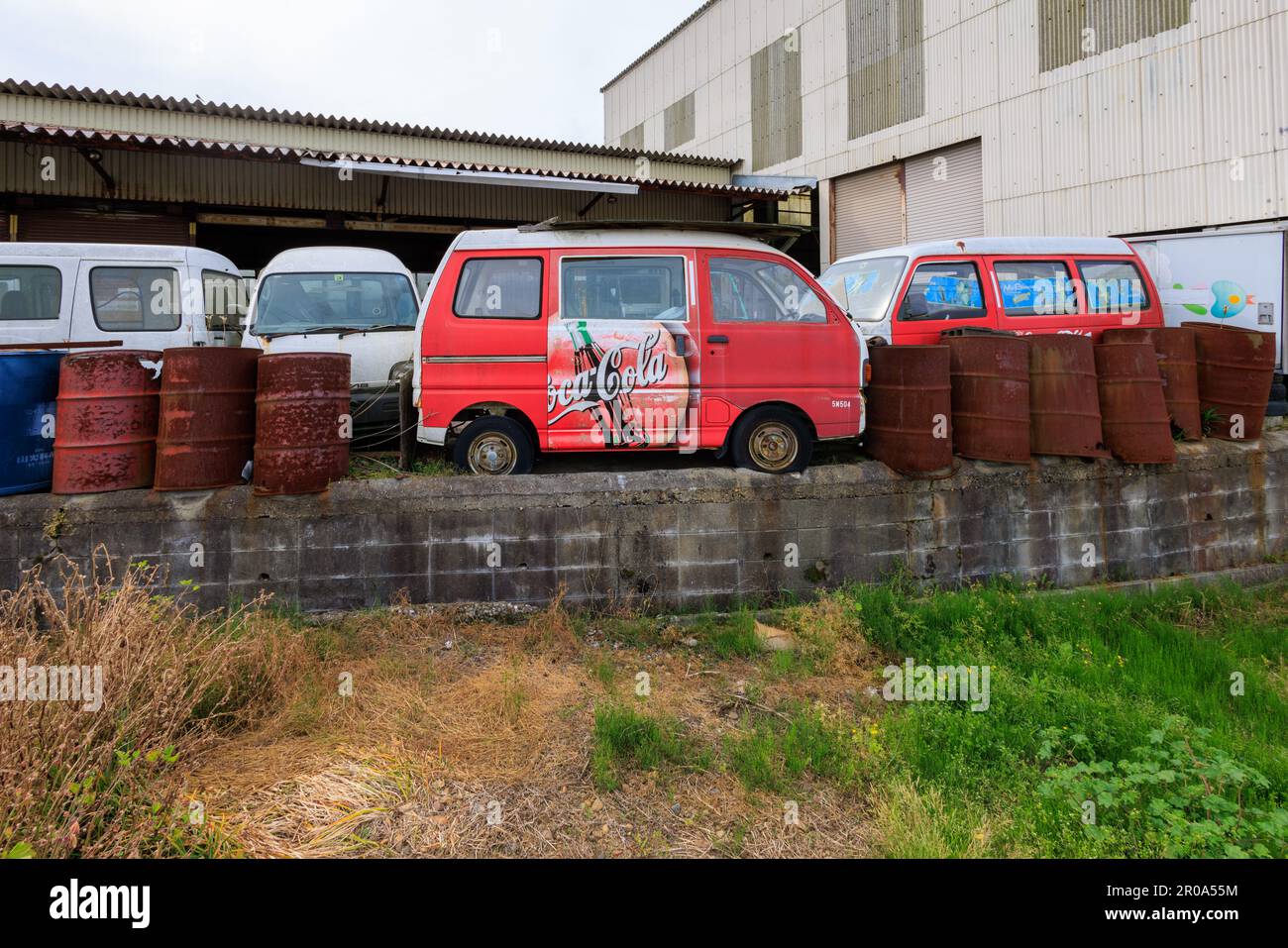 Okubo, Japan - May 6, 2023: Vintage red kei van painted with Coca Cola logo by rusted barrels Stock Photo