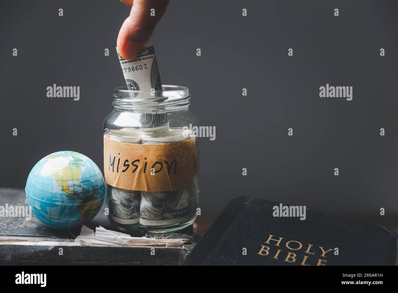 Saving jars full of money and globe with Holy Bible for mission, Mission christian idea. Hand holding dollar with bible on wooden table, Christian bac Stock Photo