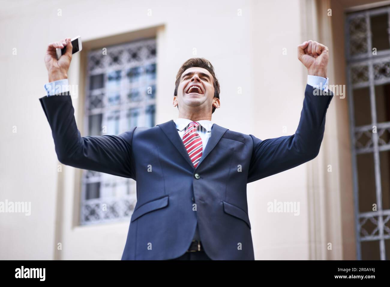Im rich. an overjoyed businessman raising his arms in victory outside a ...