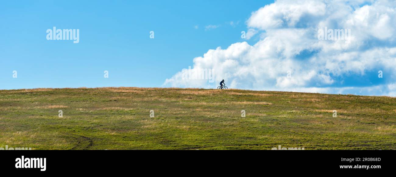 Silhouette of unrecognizable cyclist enjoying off-road cycling and mountain biking outdoor sport activity at Zlatibor hills with blue sky and clouds i Stock Photo