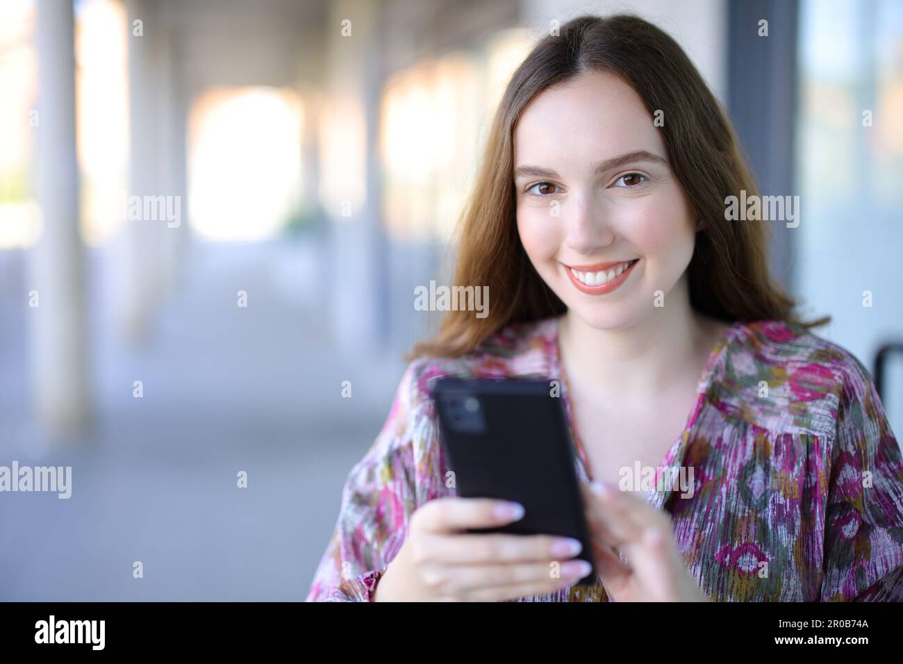 Happy woman holding cellphone looking at camera in the street Stock Photo