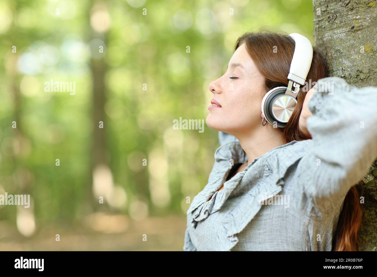 Side view portrait of a happy woman relaxing listening music in a forest Stock Photo
