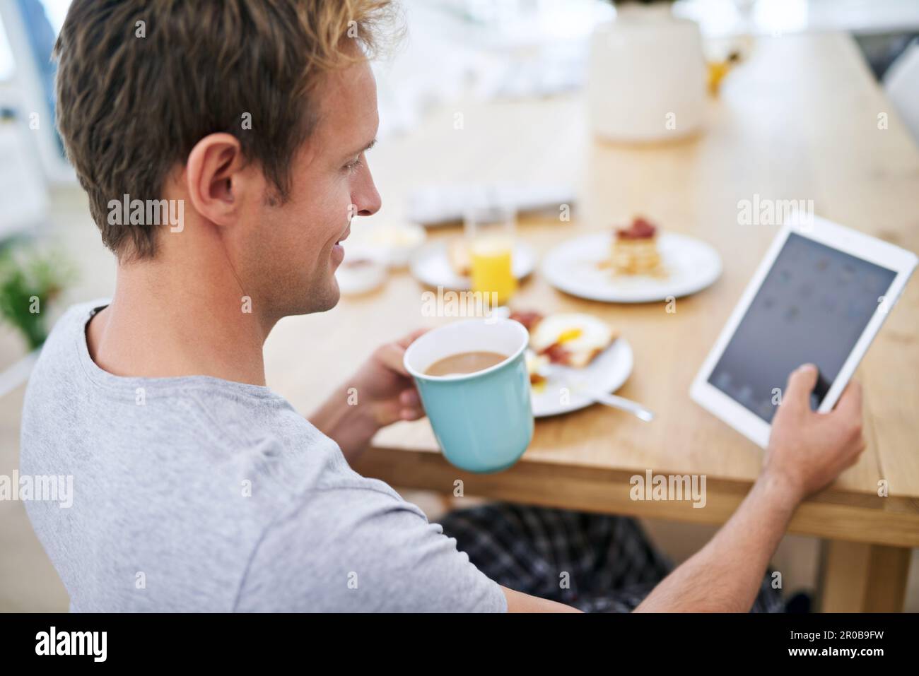 Having a relaxed breakfast. a handsome man using his tablet while having breakfast at home. Stock Photo