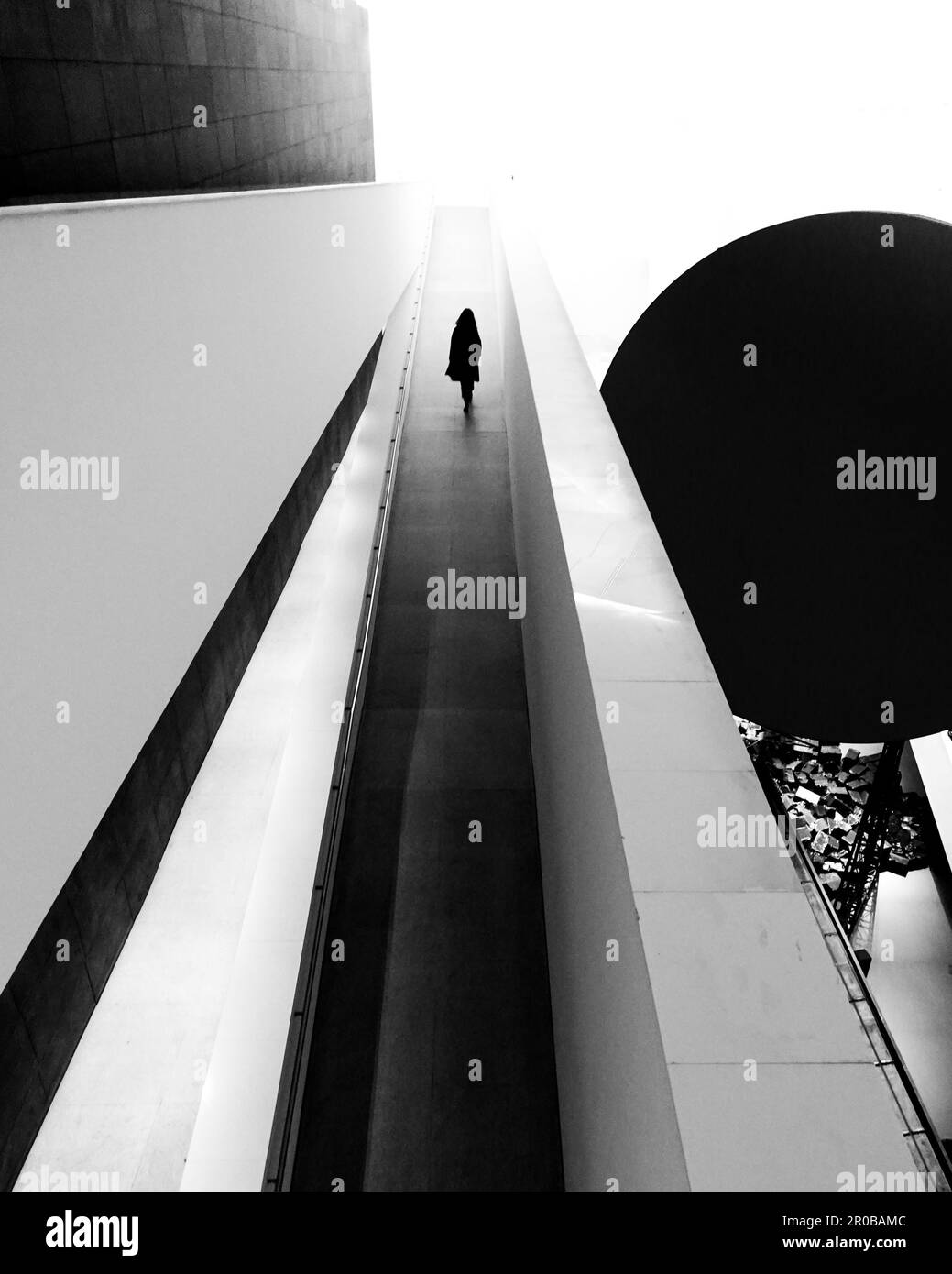A silhouetted figure walking on the rooftop of a building in grayscale Stock Photo