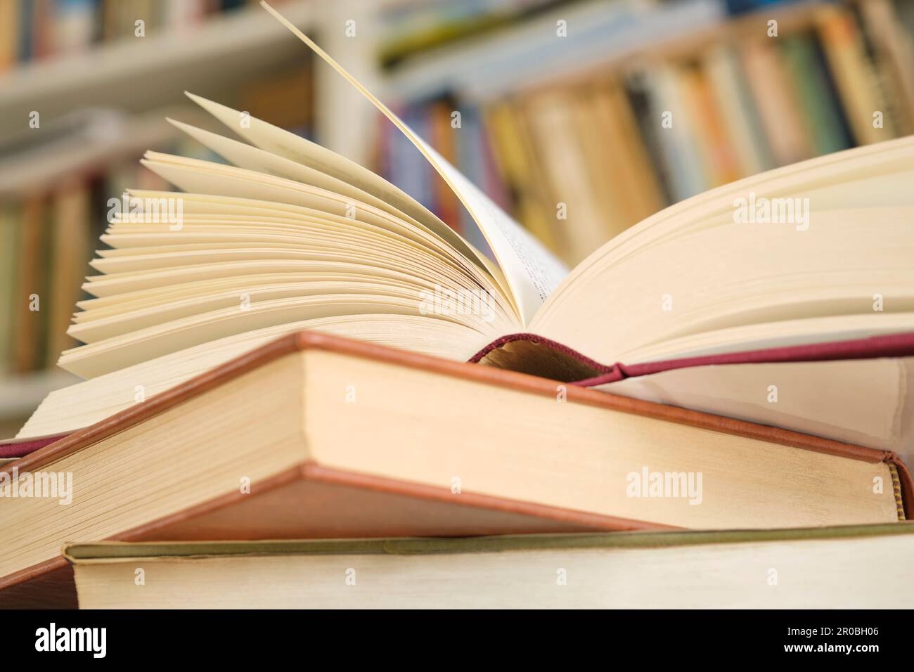 Open book or textbook on a pile of closed books in front of a bookcase in a library. Education learning concept. Image with selective focus. Stock Photo