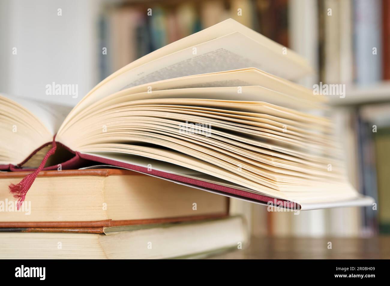 Open book or textbook on a pile of closed books in front of a bookcase in a library. Education learning concept. Image with selective focus. Stock Photo
