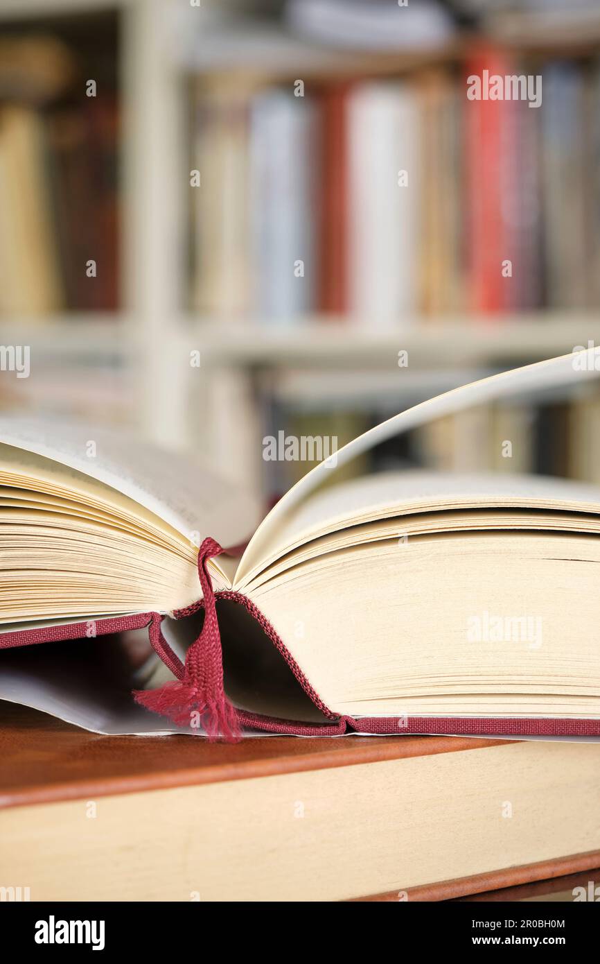 Open book or textbook on a pile of closed books in front of a bookcase in a library. Education learning concept. Vertical image with selective focus. Stock Photo