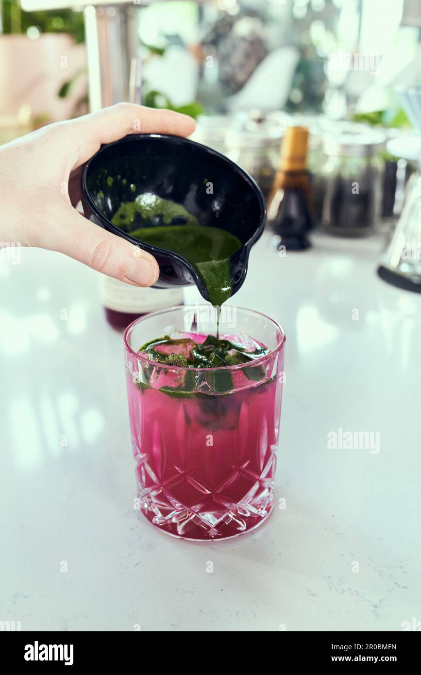 A hand pours matcha green tea into prickly pear lemonade. Stock Photo