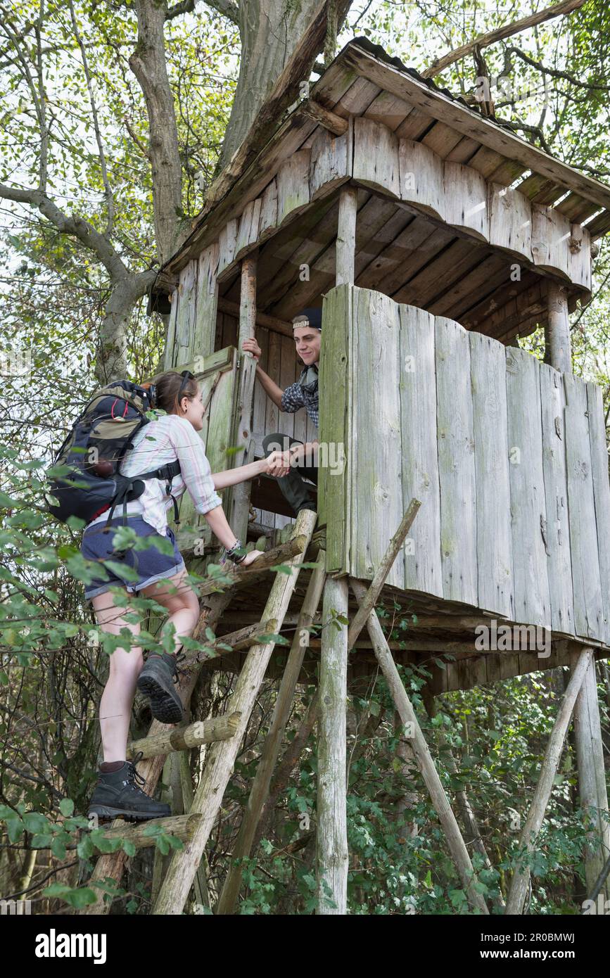 Teenage hiker helping woman to climb on lookout tower in a forest, Bavaria, Germany Stock Photo