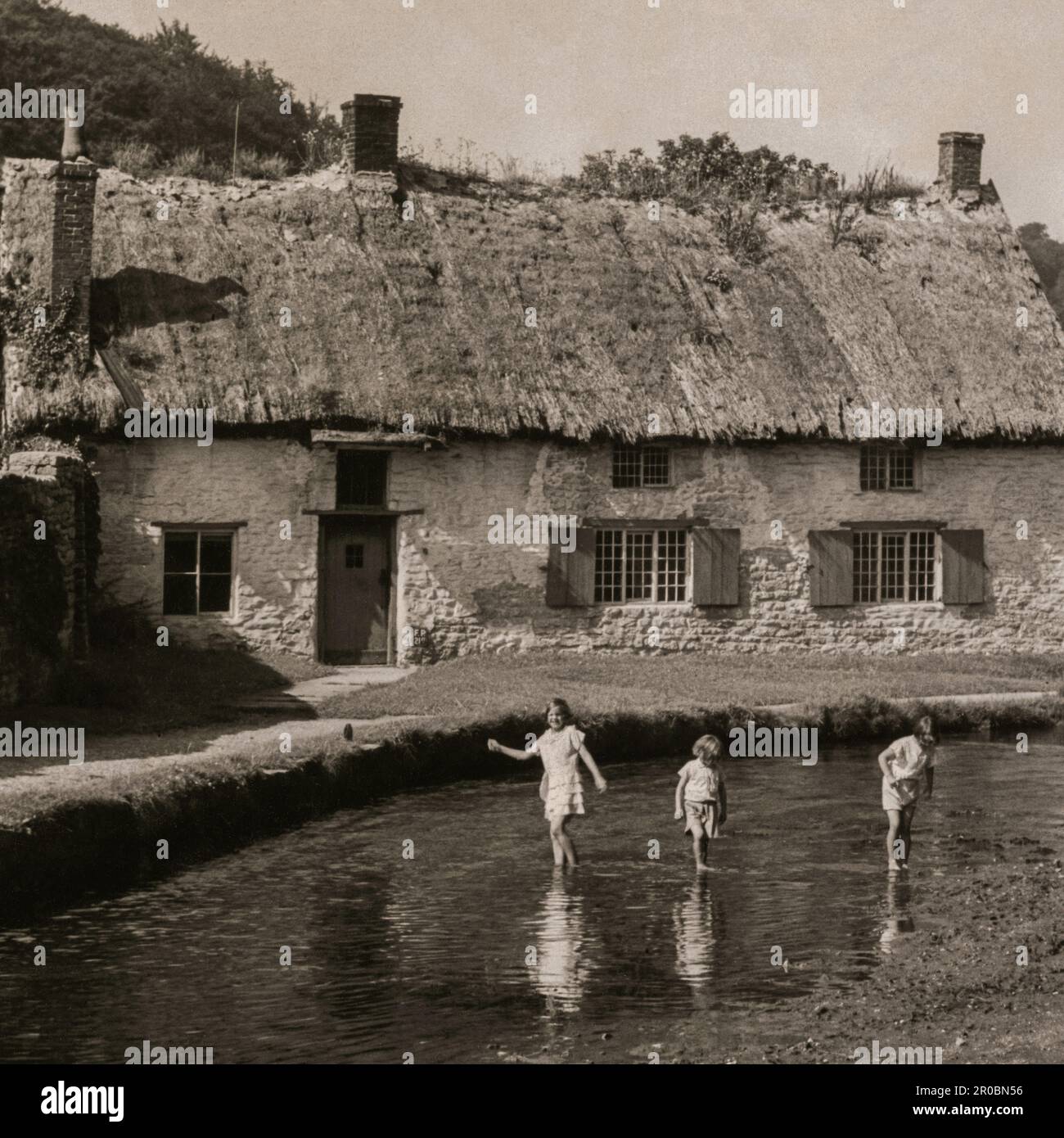 Photograph taken in the 1930s of Beck Isle Cottage, also known as The Thatched Cottage, in Thornton-le-Dale, Yorkshire, England.  The cottage was built in the 1600s of cruck construction. In this image, the thatch is rotten and the roof in need of re-thatching. Bushes and grass appear to be growing out of the roof ridge. Stock Photo