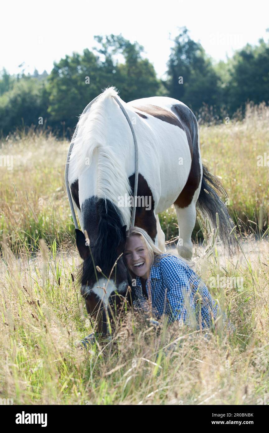 Mid adult woman stroking her horse on meadow and smiling, Bavaria, Germany Stock Photo