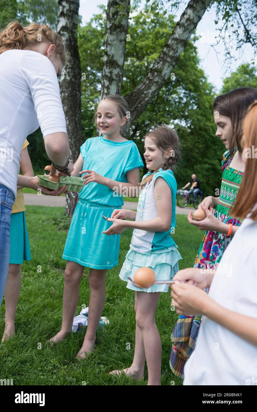 Female trainer distributing eggs to kids for spoon race in a park, Munich, Bavaria, Germany Stock Photo