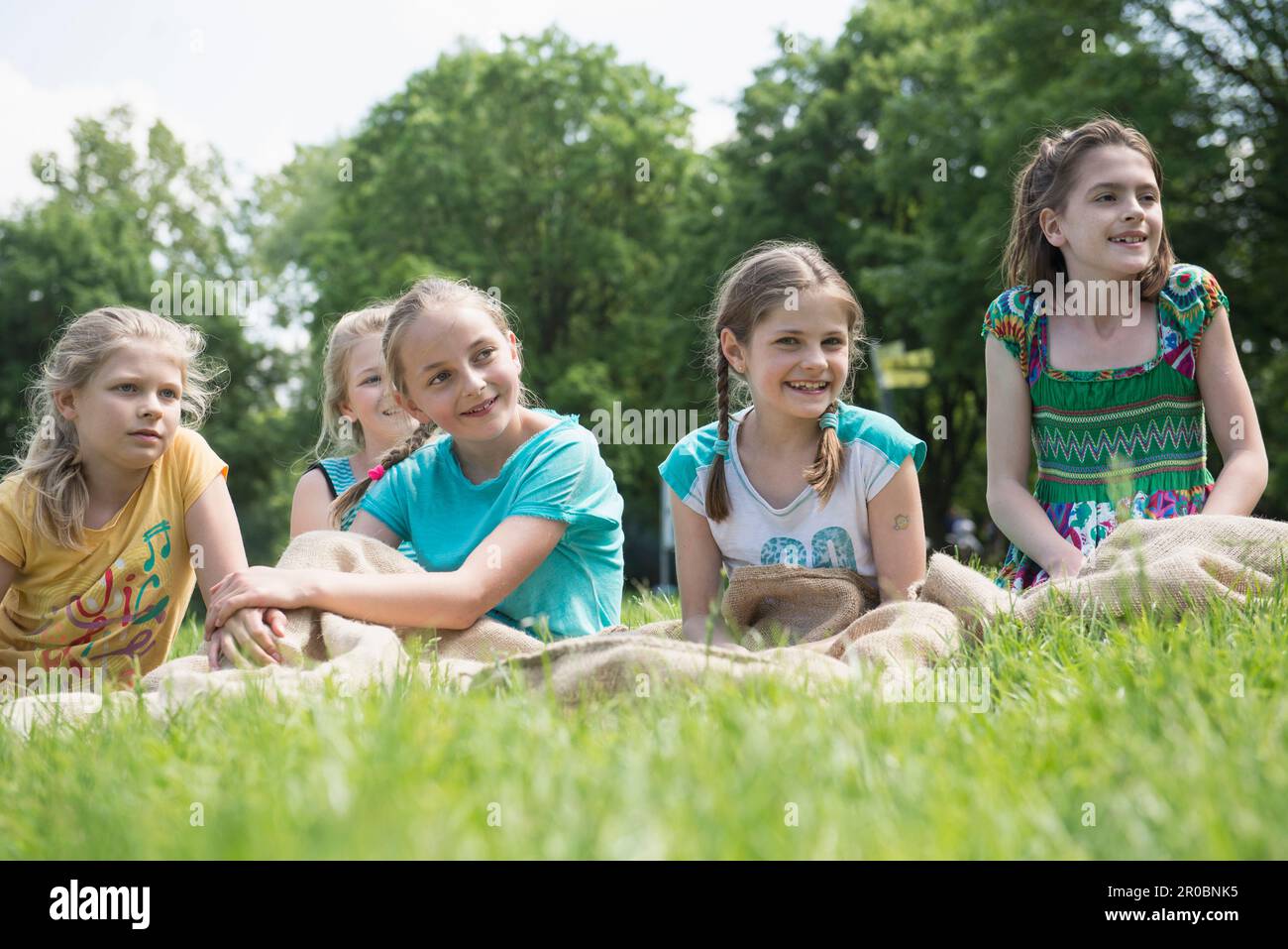 Group of children sitting on meadow and have a rest after sack race, Munich, Bavaria, Germany Stock Photo
