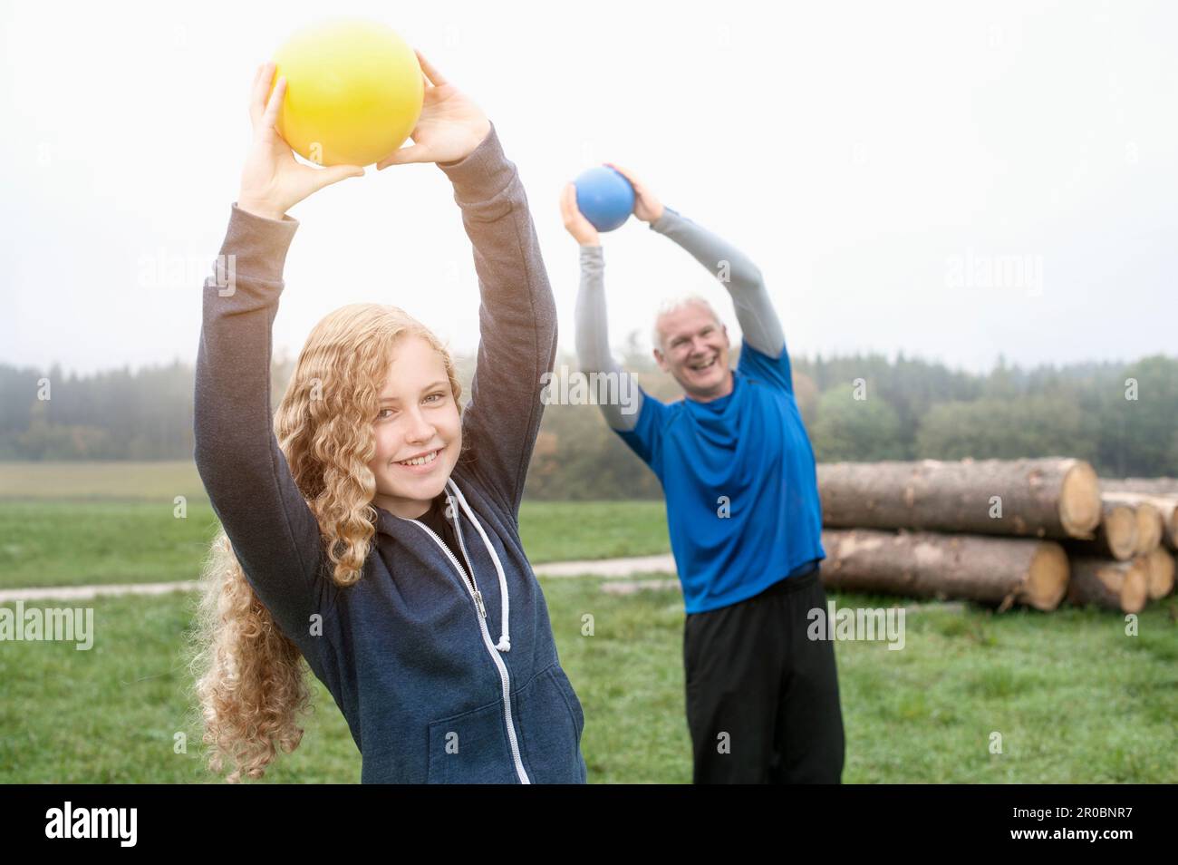 Teenage Girl with her father exercising with yoga ball on the field and smiling during dawn, Bavaria, Germany Stock Photo