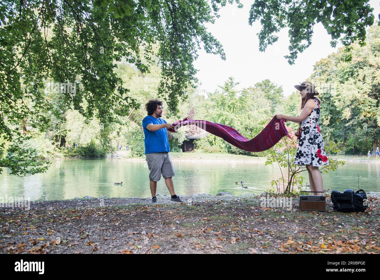 Couple spread out blanket for picnic at lakeshore in the English Garden