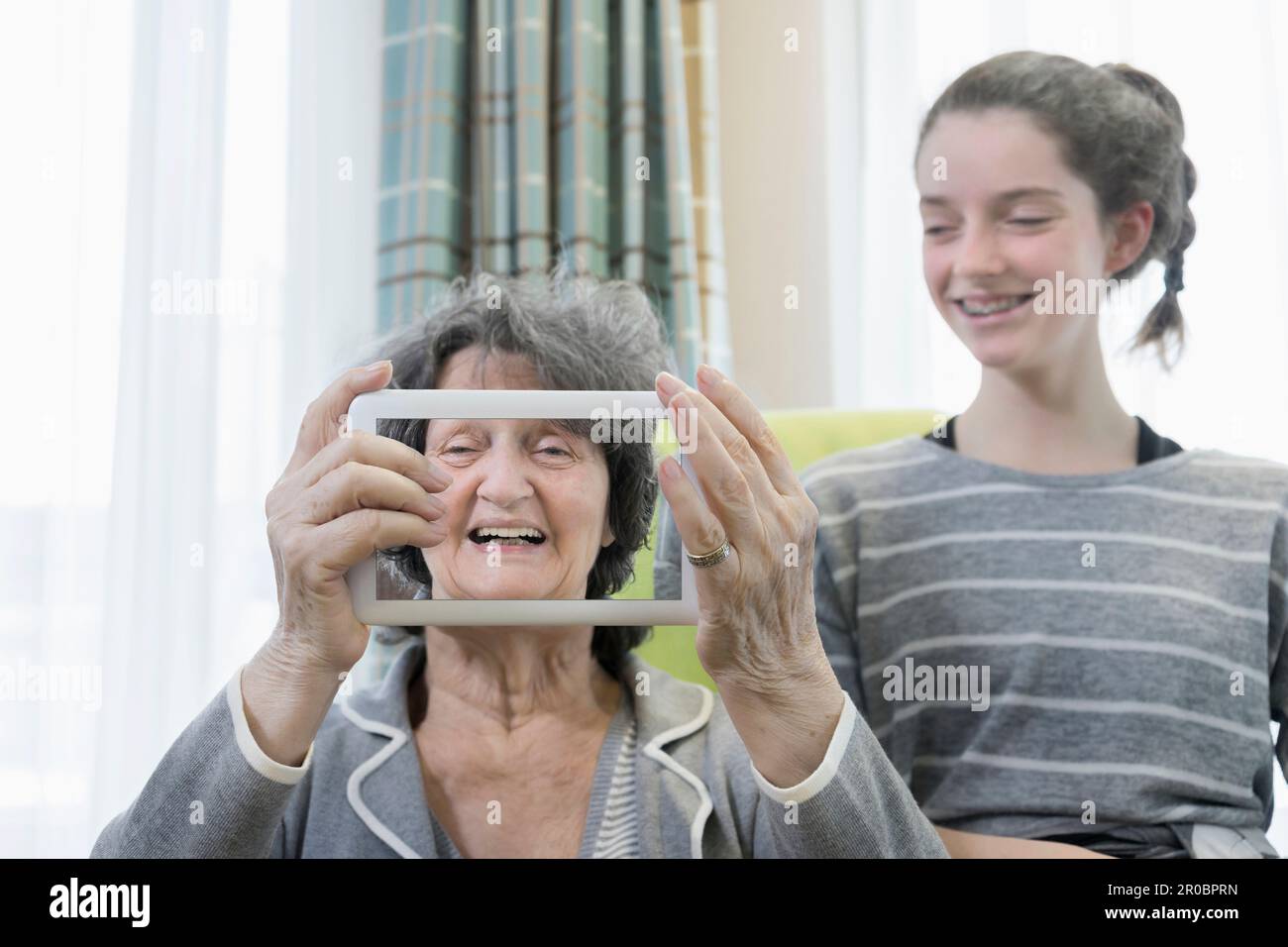 Senior woman with granddaughter taking photos using digital tablet at rest home Stock Photo