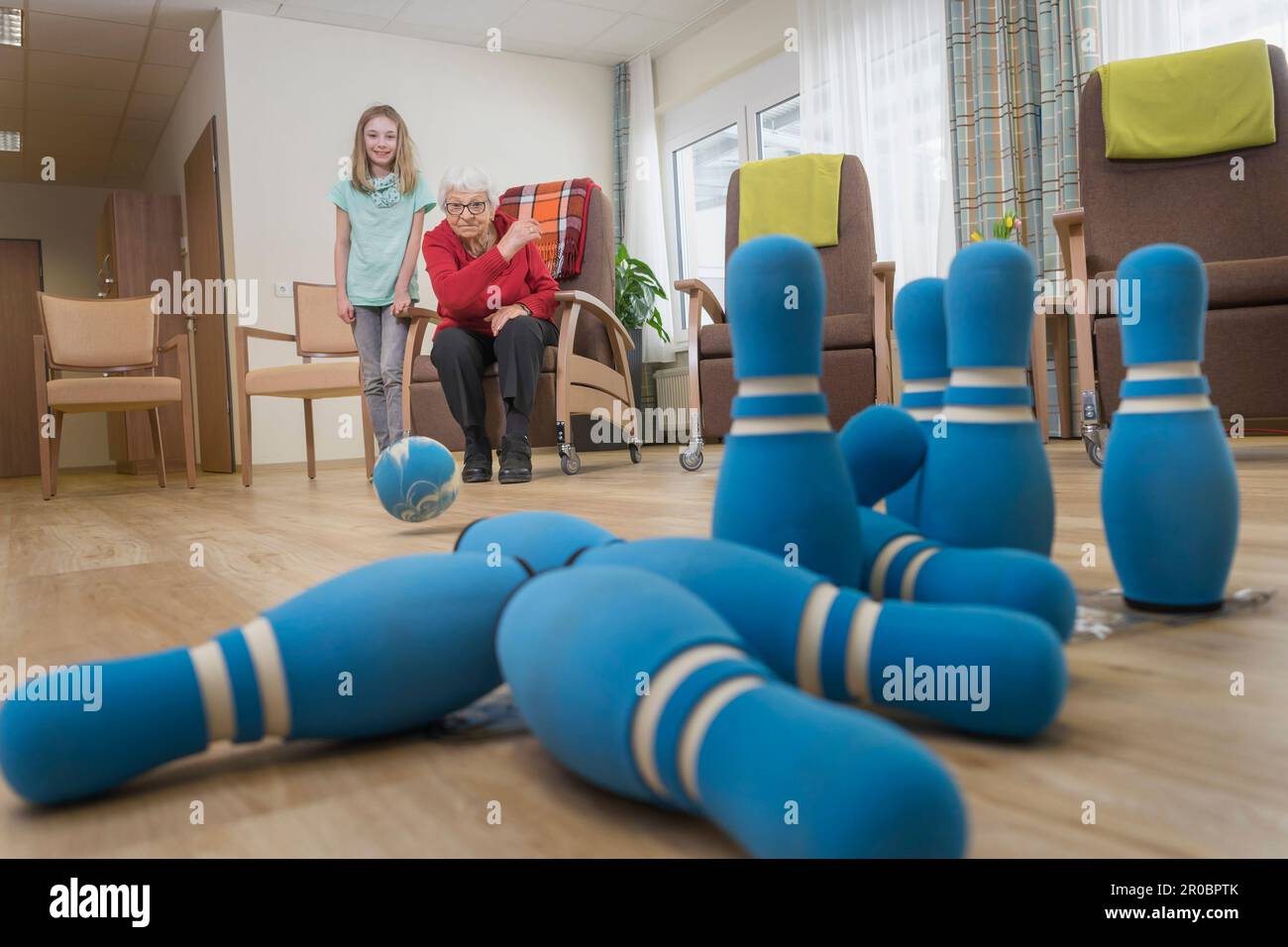 Girl playing bowling with senior woman in rest home Stock Photo
