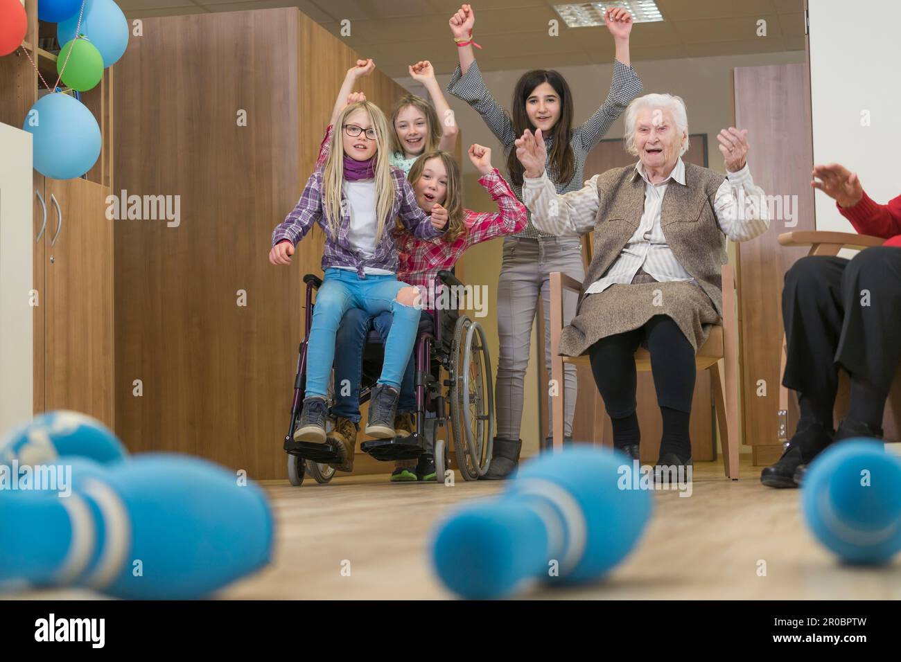 Girls playing bowling with senior woman in rest home Stock Photo