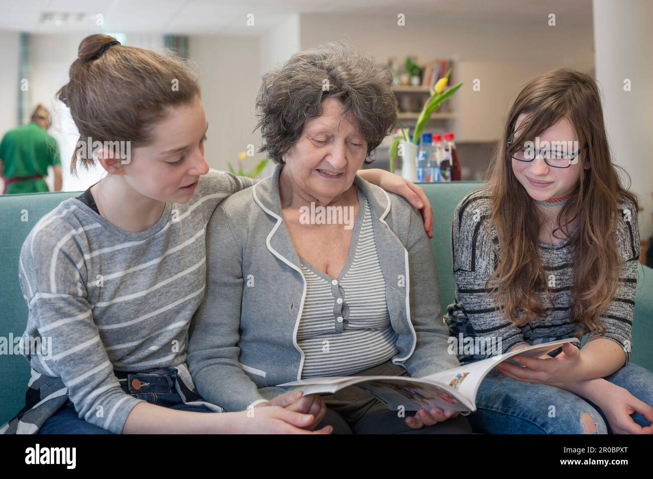 Girls reading magazine with senior woman in rest home Stock Photo