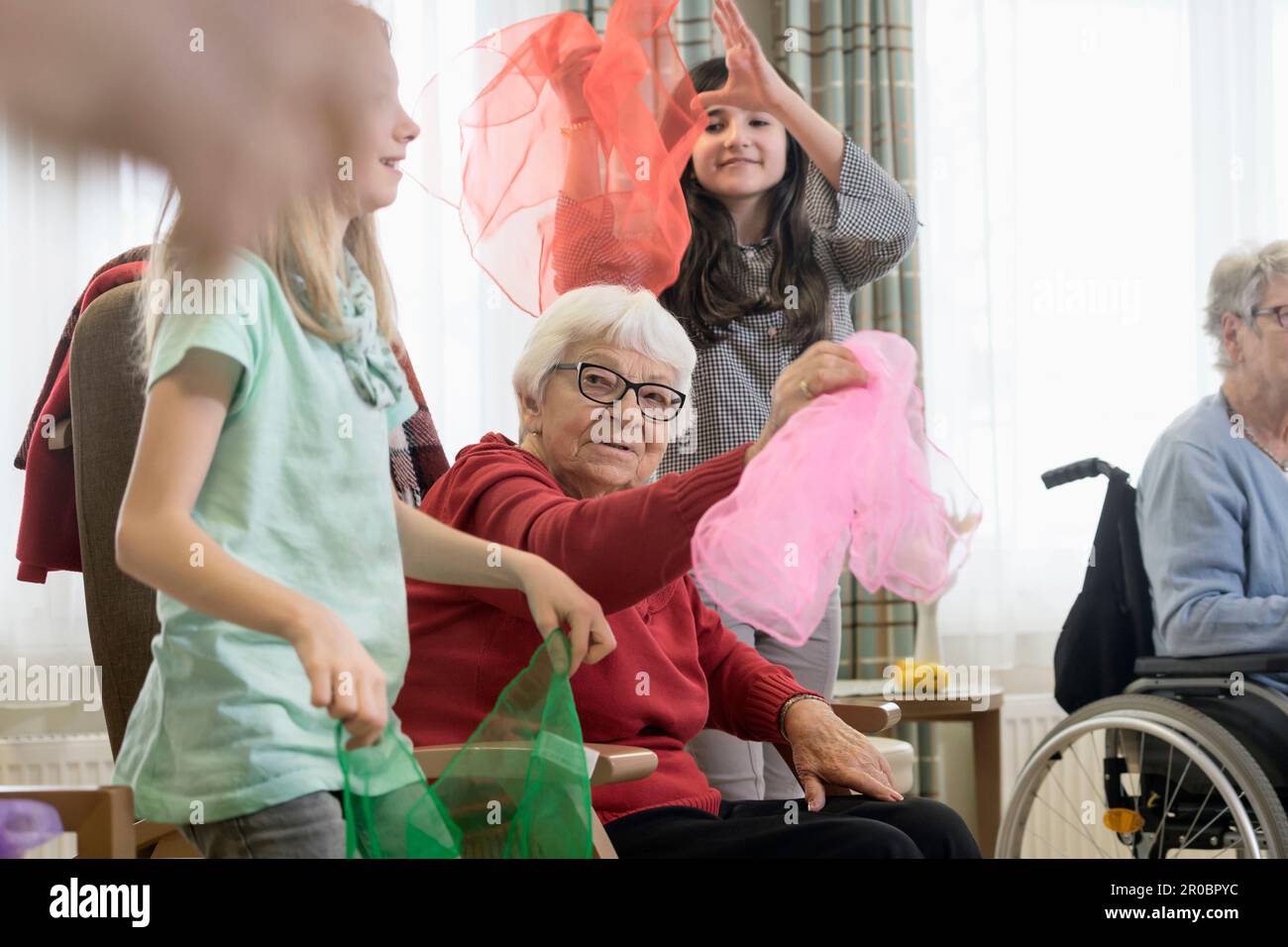 Girls with senior woman doing gentle sports exercise with cloth in rest home Stock Photo