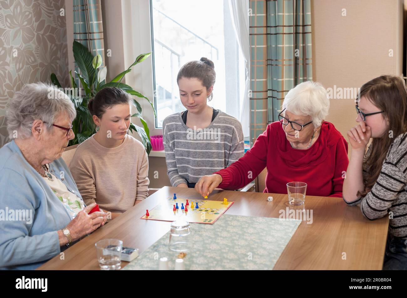 Girls playing ludo board game with senior women in rest home Stock Photo