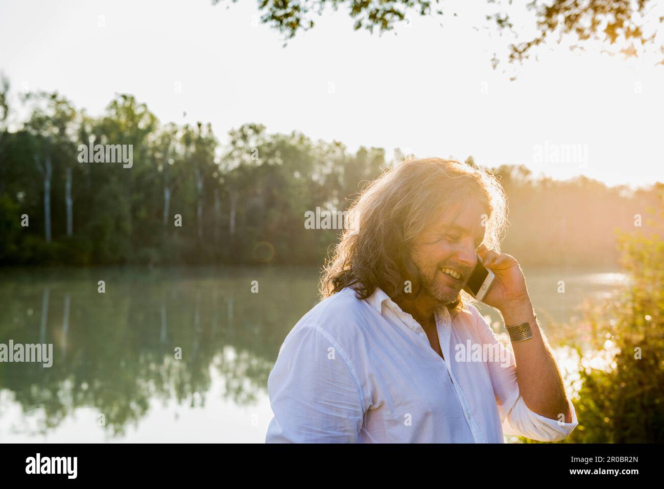 Man talking on mobile phone at riverbank, Bavaria, Germany Stock Photo