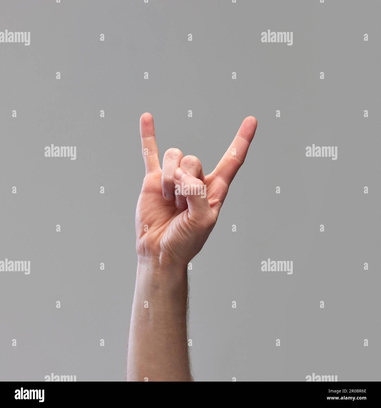 Male hand showing gesture of rock and roll, Hook 'Em Horns against grey