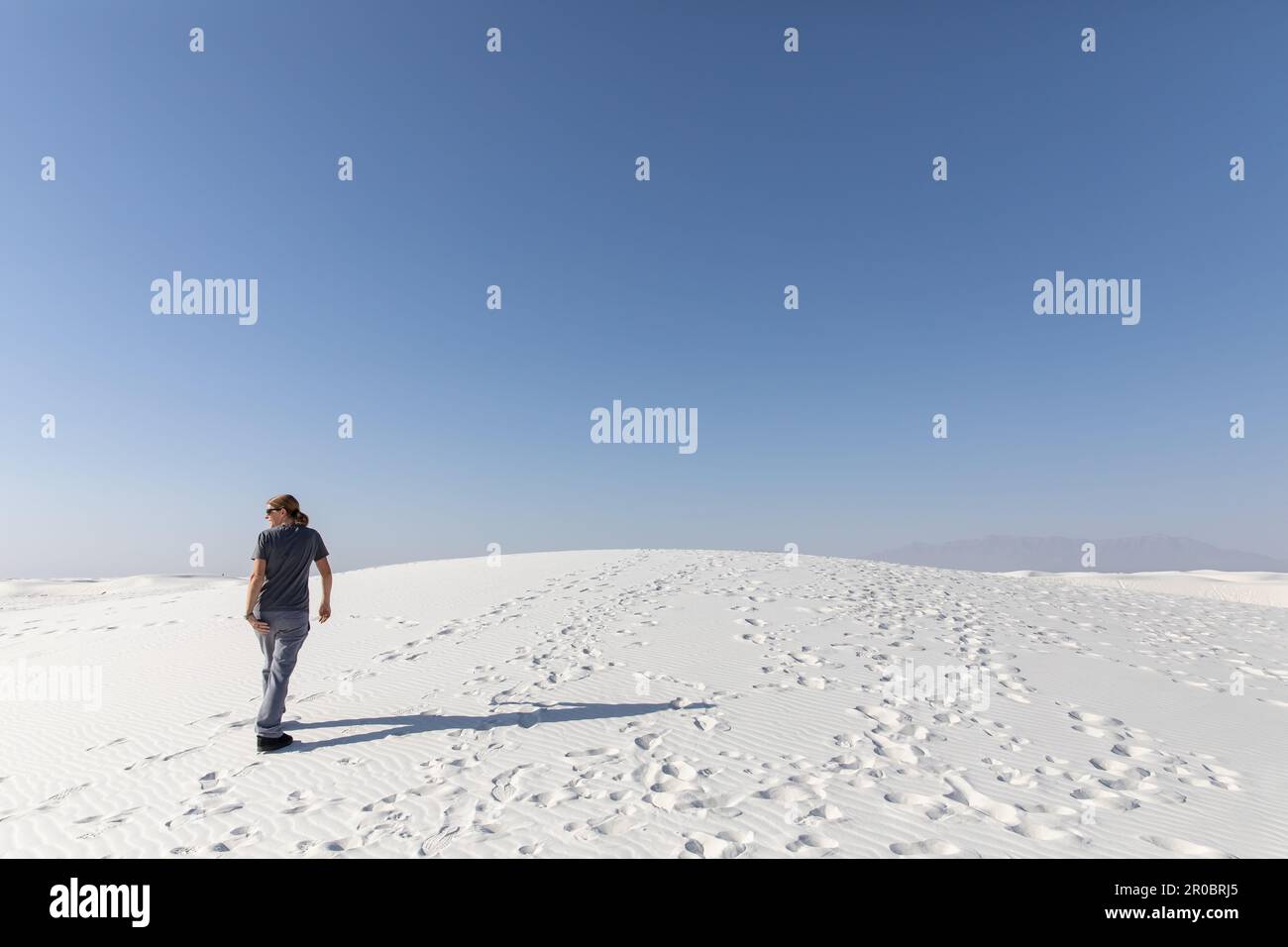 Woman walking away from camera over white sand dune Stock Photo