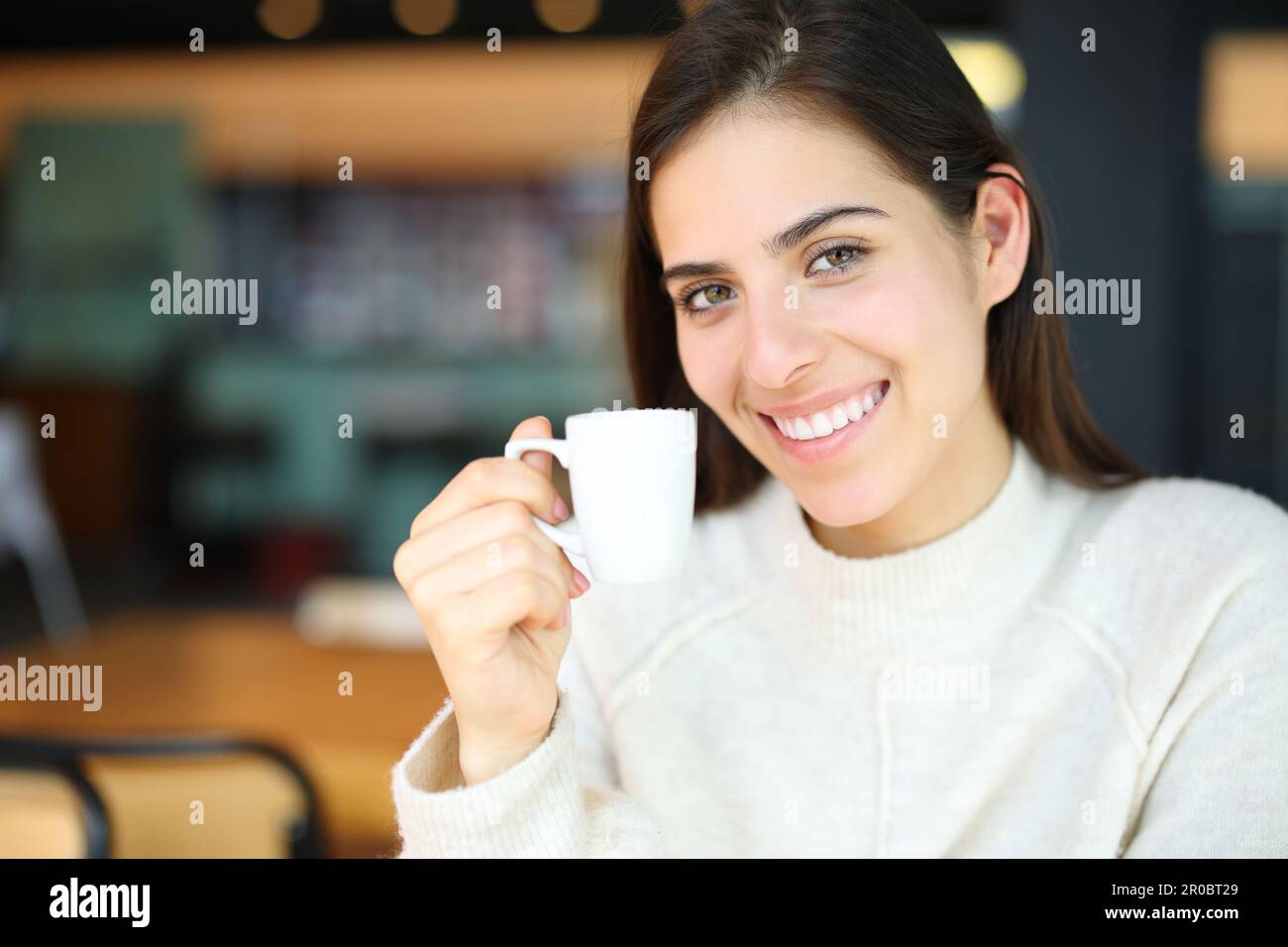 Happy woman smiling holding coffee cup in a bar looking at camera Stock Photo