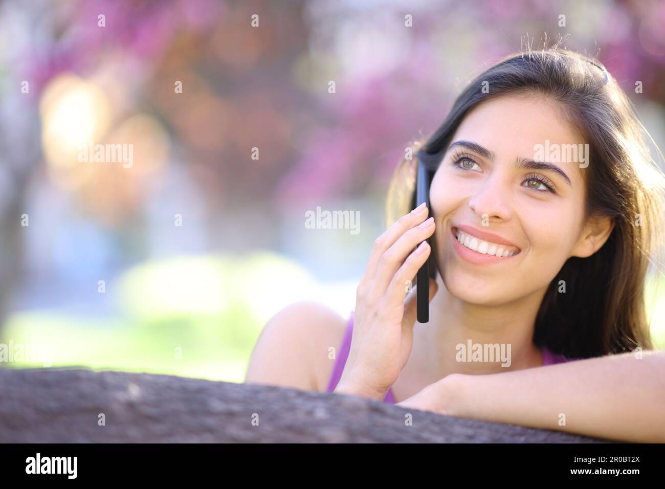 Front view portrait of a beautiful happy woman calling on phone in spring in a park Stock Photo