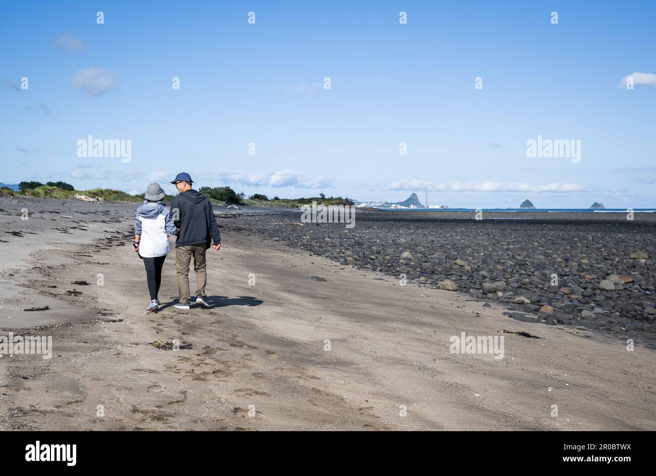 Couple holding hands and walking on the beach. Sugar Loaf Islands in the distance. New Plymouth. Stock Photo