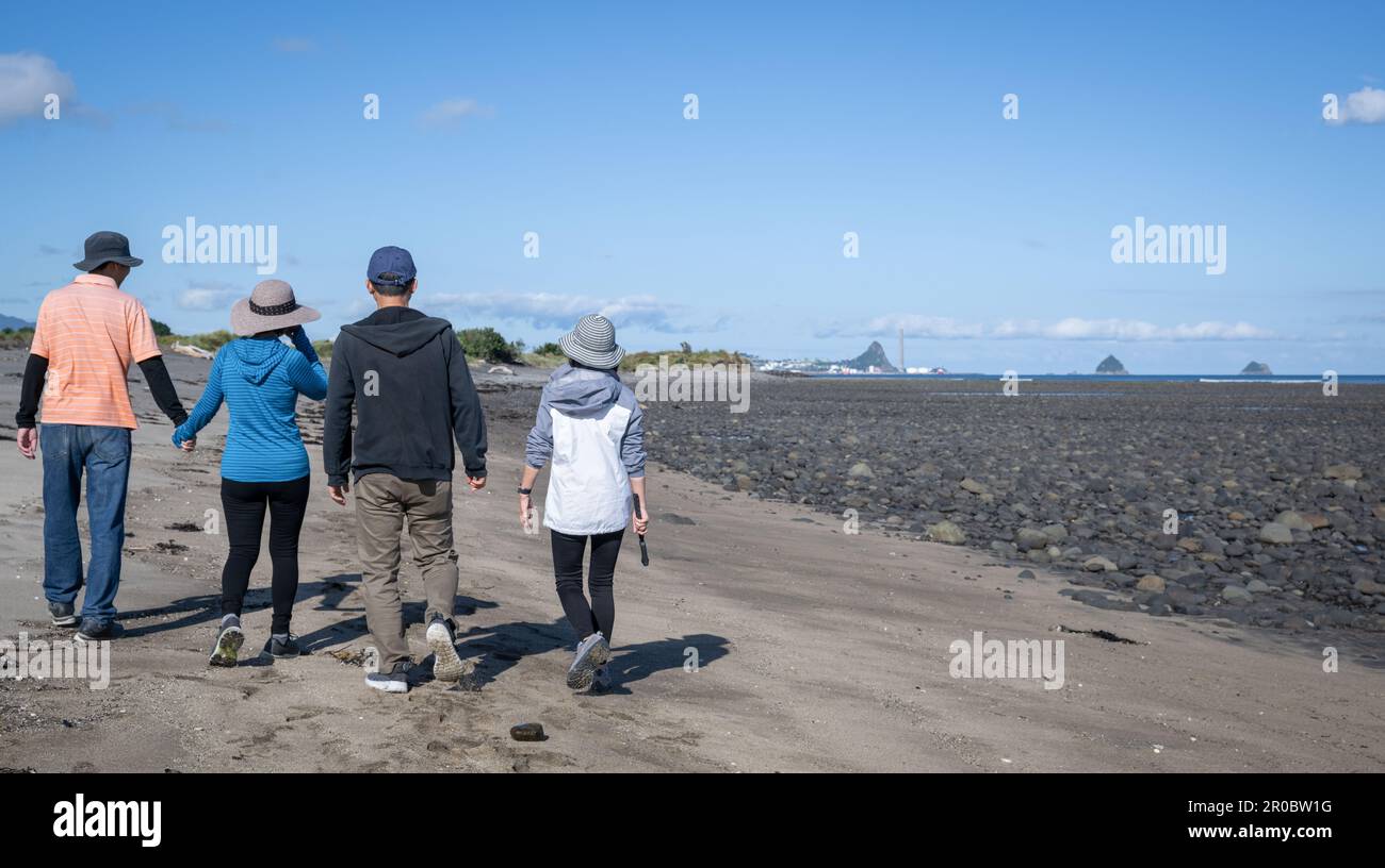 Four people walking on the beach. Sugar Loaf Islands in the distance. Tourists having fun. New Plymouth. Stock Photo