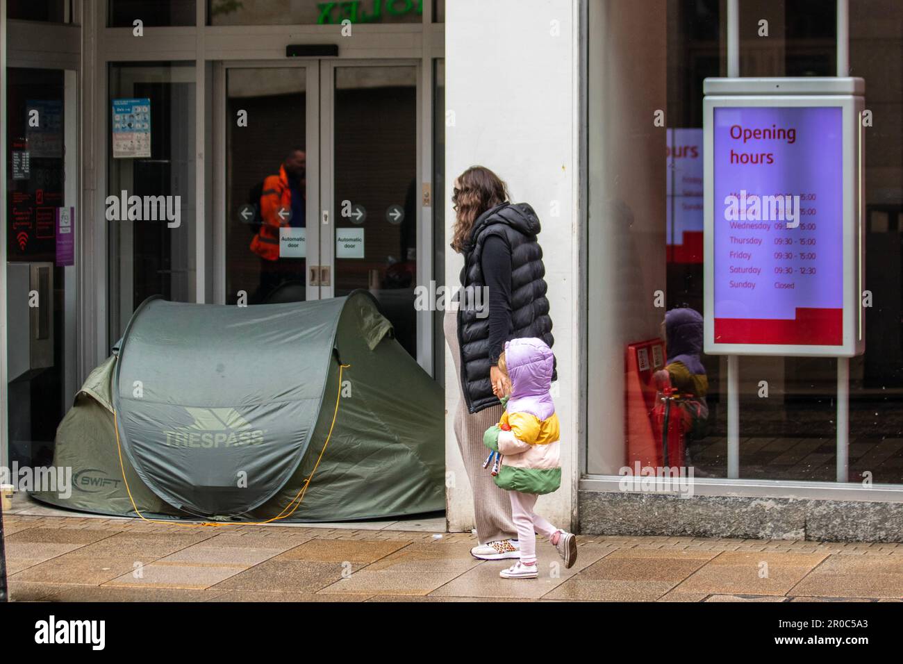 'Opening Hours' Banking digital signage in Preston, Lancashire.  8 May 2023 UK weather. Rough sleeper, having erected a tent in the doorway of SANTANDER Bank. Shops, shoppers shopping on a Wet and windy  Bank Holiday Monday in Preston.  Credit; MediaWorldImages/AlamyLiveNews Stock Photo