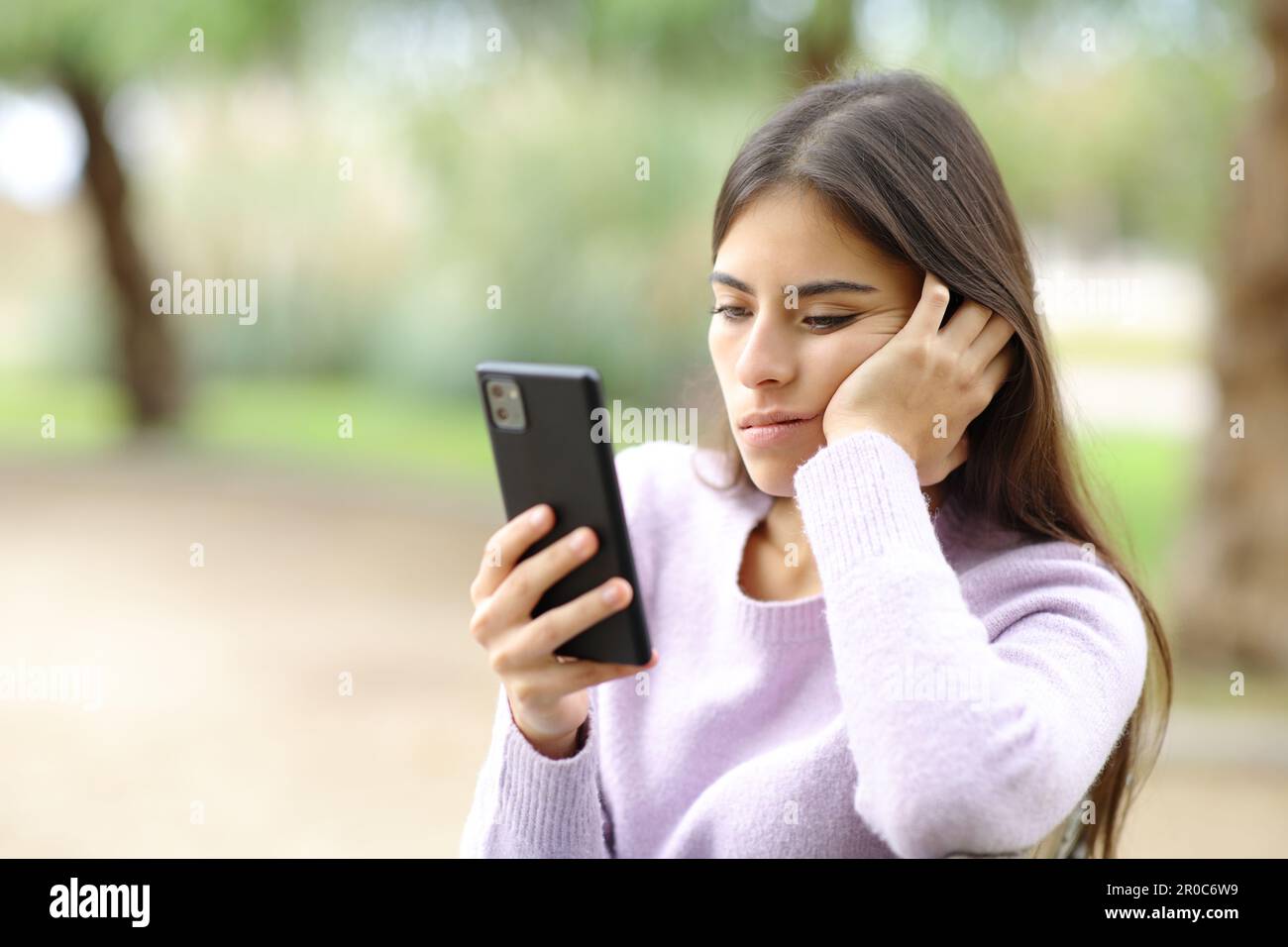 Bored woman checks smart phone sitting in a park Stock Photo