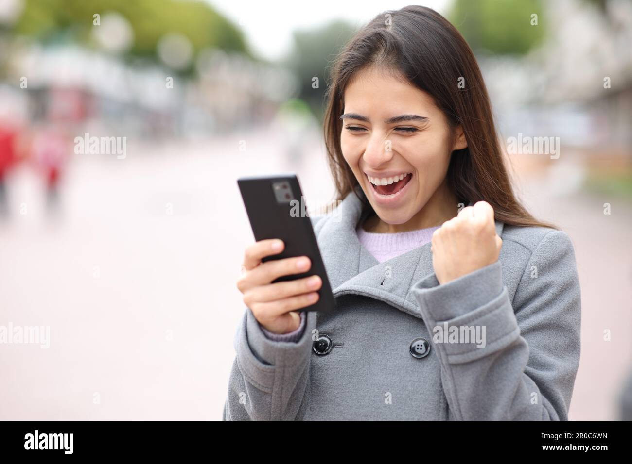 Excited woman checking content on phone in the street Stock Photo