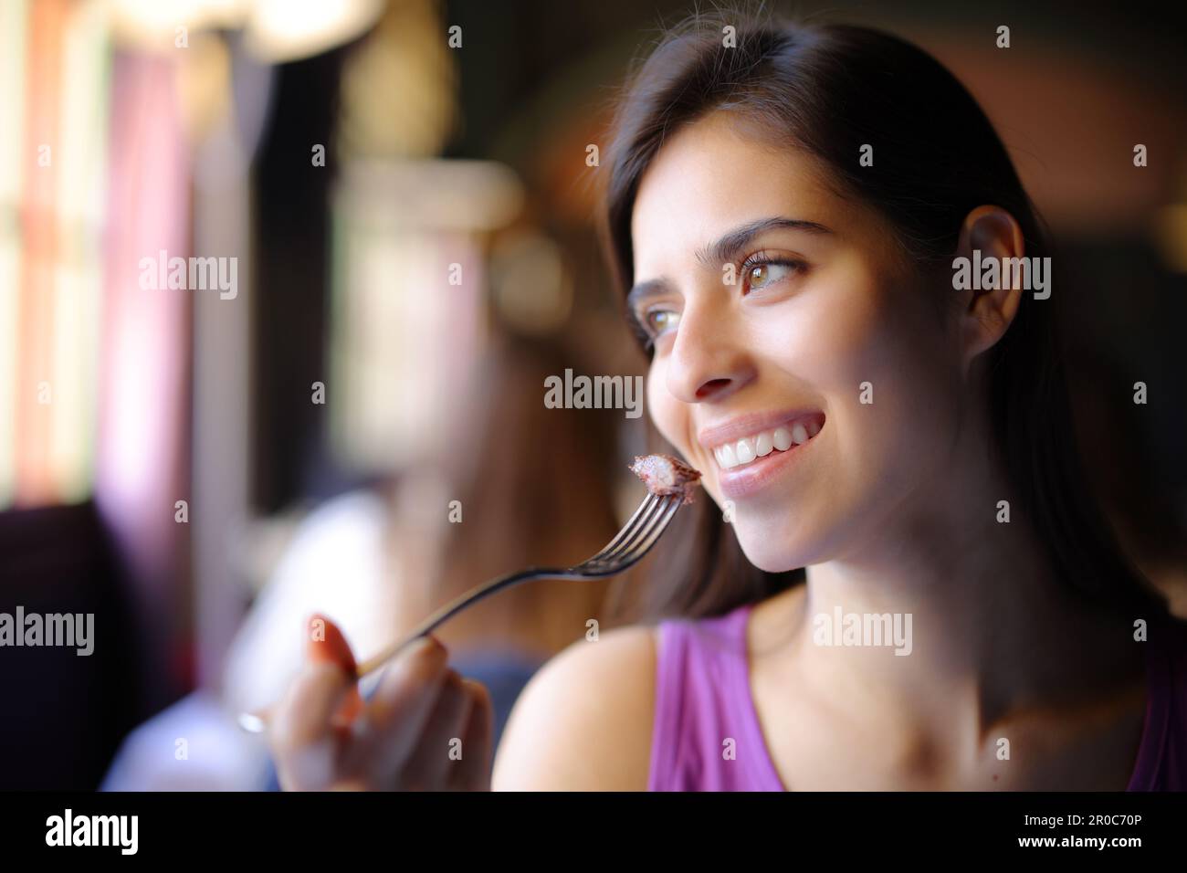 Happy woman eating meat in a restaurant looking away Stock Photo Alamy