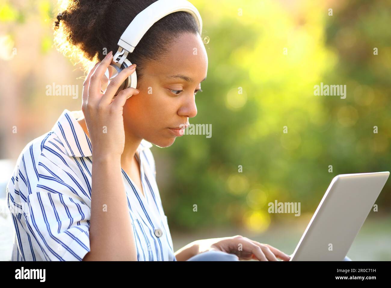 Serious black woman wearing headphone watching video on laptop in a park Stock Photo